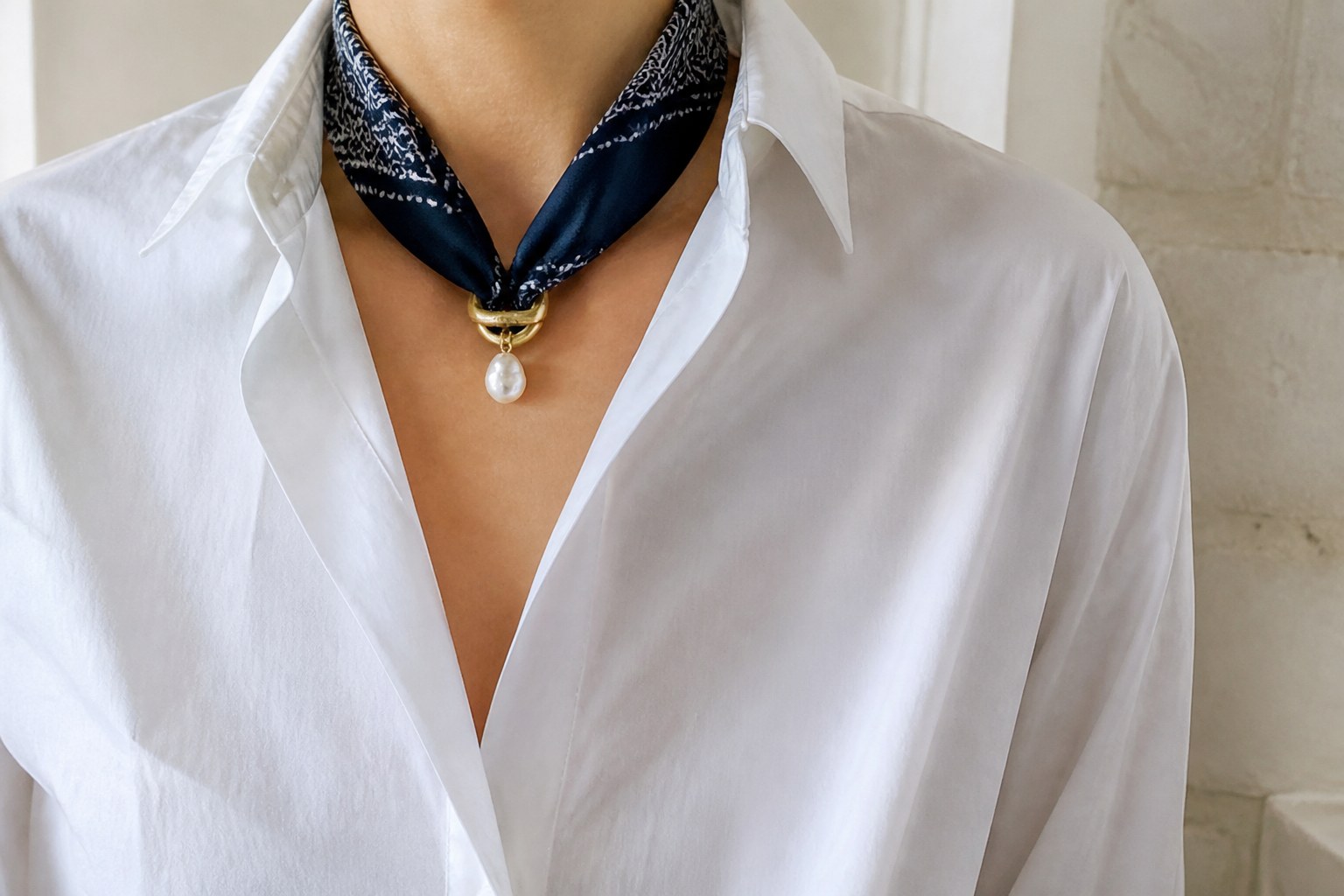 Navy silk bandana necklace held by an aged-gold ring and irregular pearl over a white cotton shirt