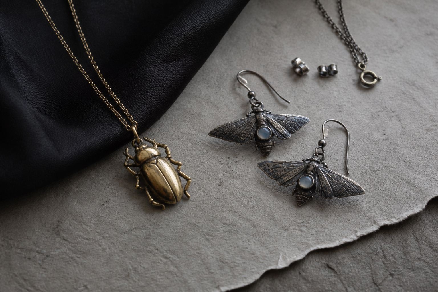 Patinated gold beetle pendant and oxidised silver moth earrings with moonstone details on handmade paper and black silk