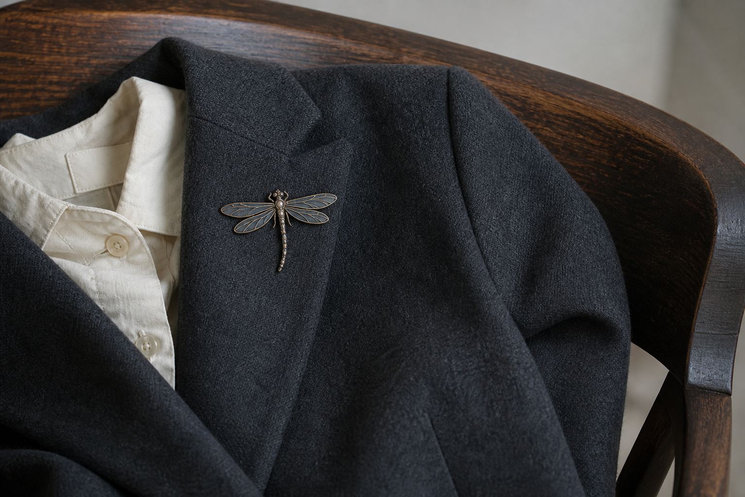 Antique-inspired dragonfly brooch pinned high on a charcoal dry-wool blazer over an ivory cotton shirt