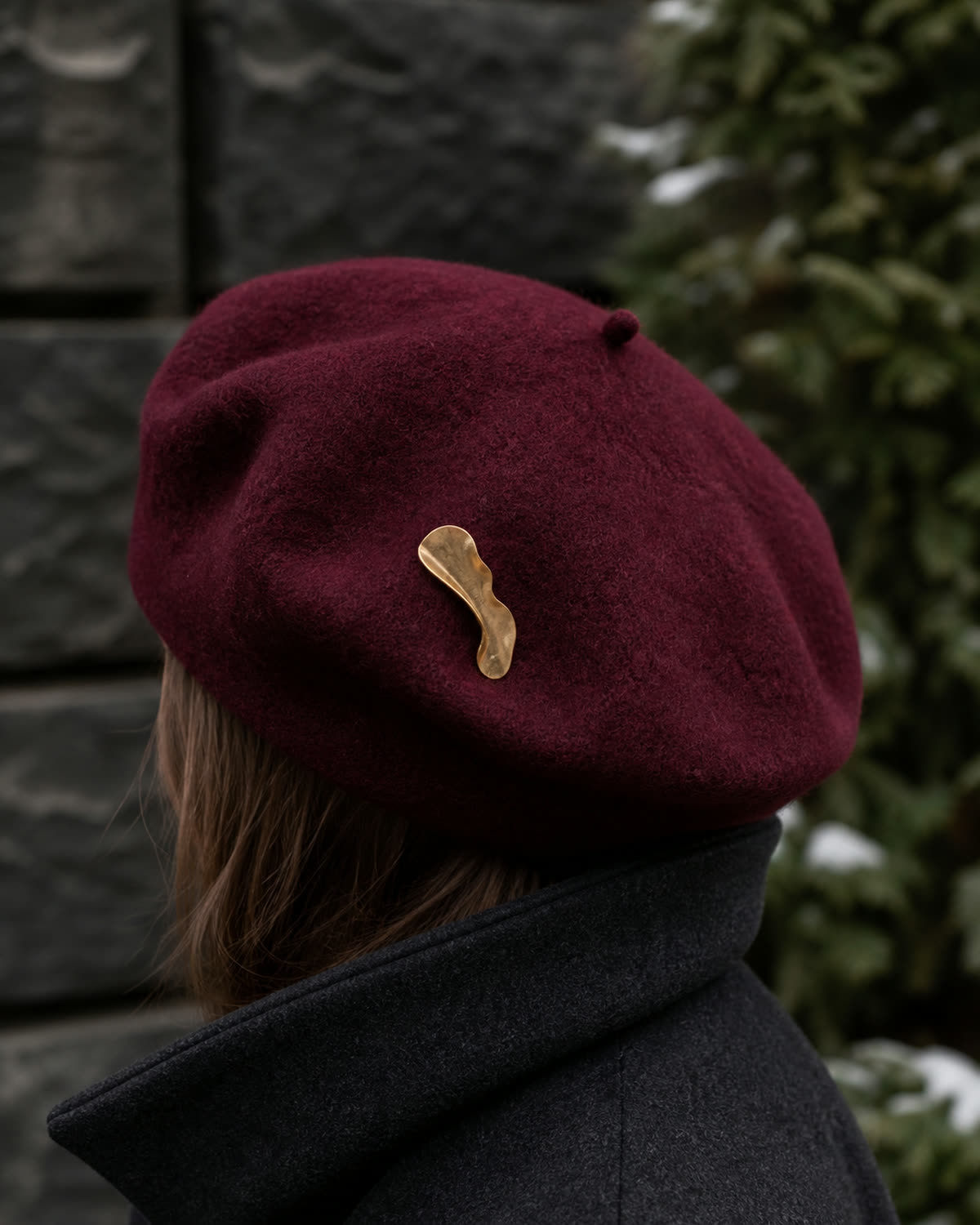 Abstract antique-gold brooch placed off-centre on an oxblood wool beret