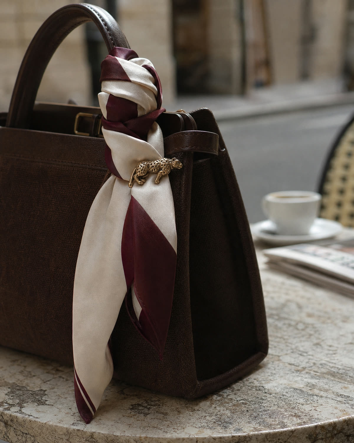Antique-gold animal brooch fastened to an oxblood-and-cream scarf tied around a brown handbag handle