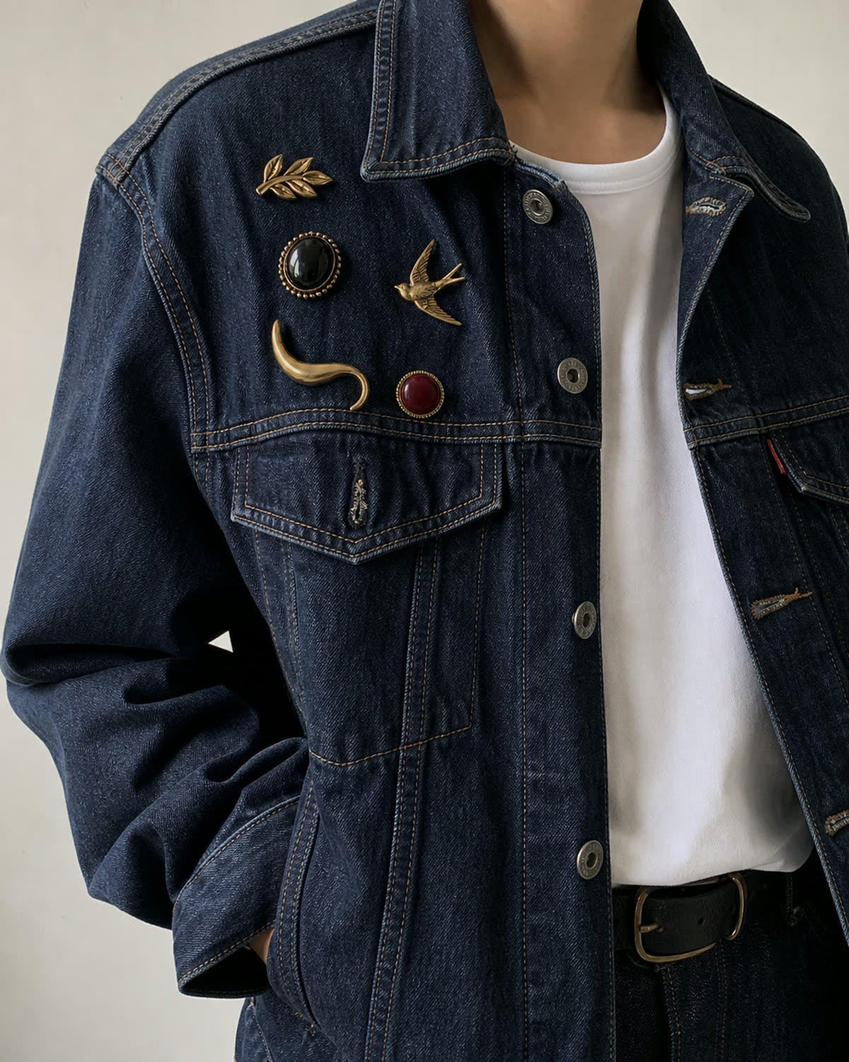 Five different antique-gold brooches clustered across a dark indigo denim jacket