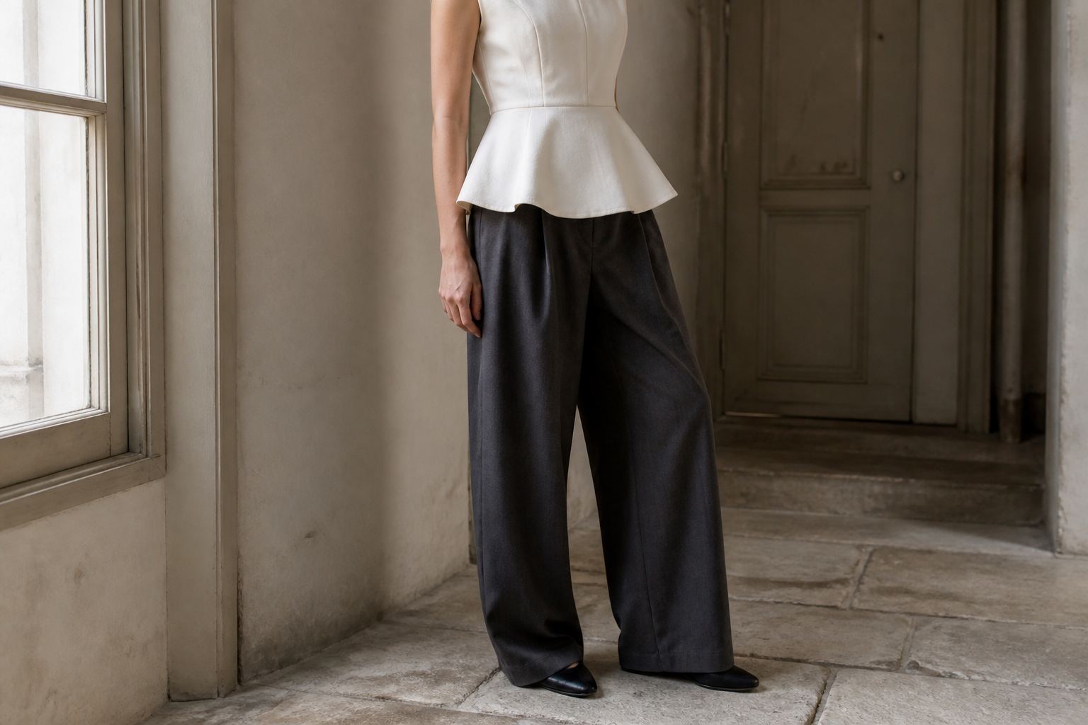 Faceless outfit with a sculptural ivory peplum top, charcoal wide trousers and black flats