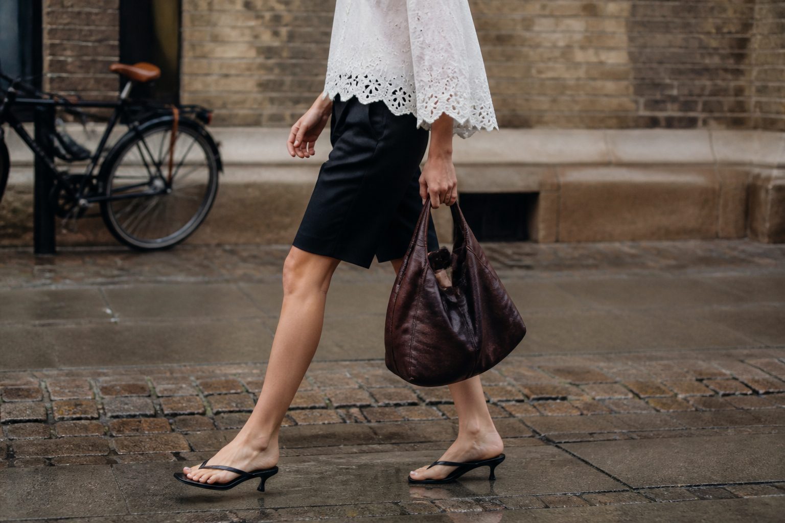Faceless Copenhagen street-style look with an ivory eyelet blouse, black Bermuda shorts and oxblood leather bag