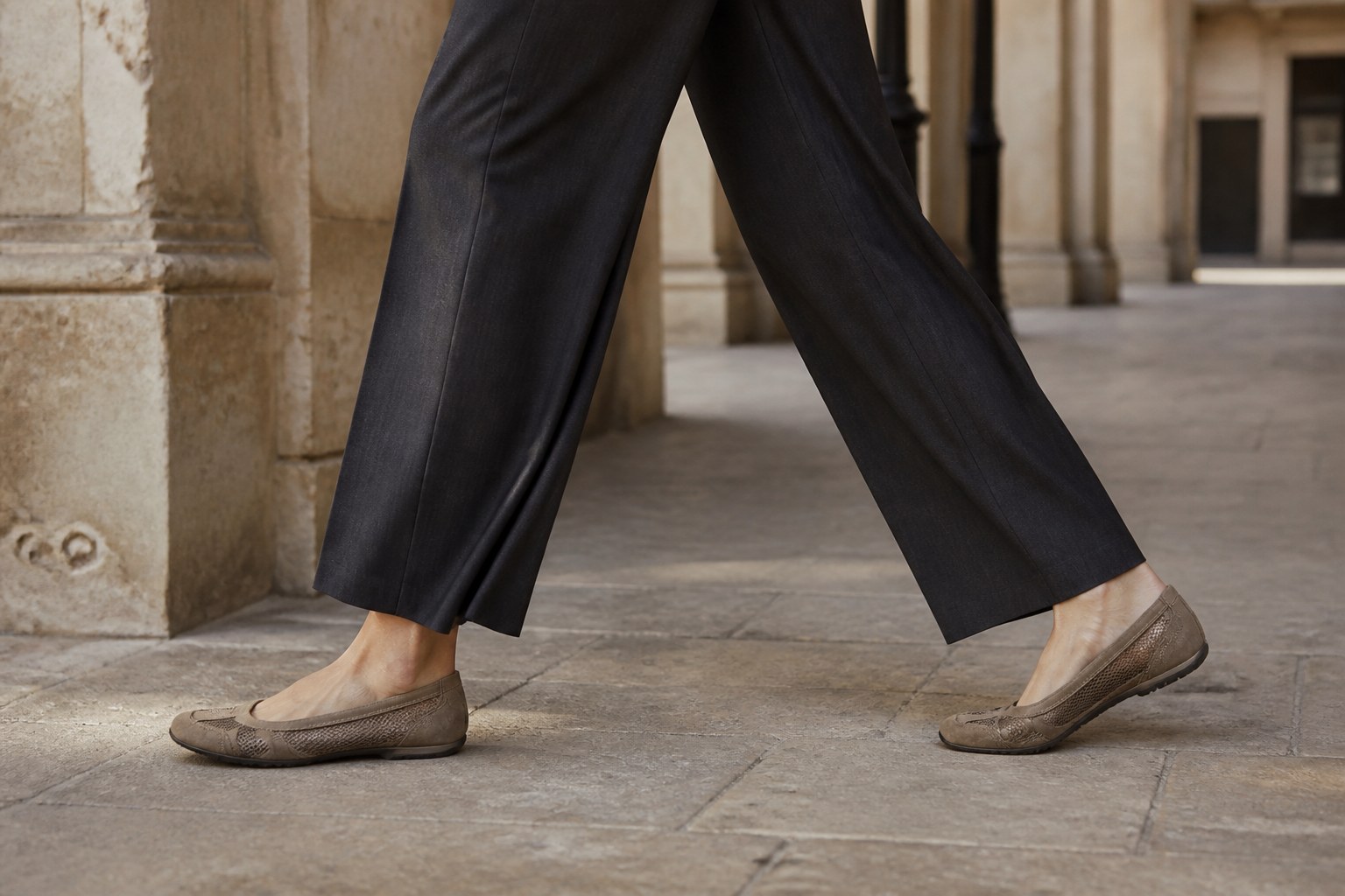 Taupe mesh and suede runner flats worn with fluid charcoal trousers in a limestone arcade