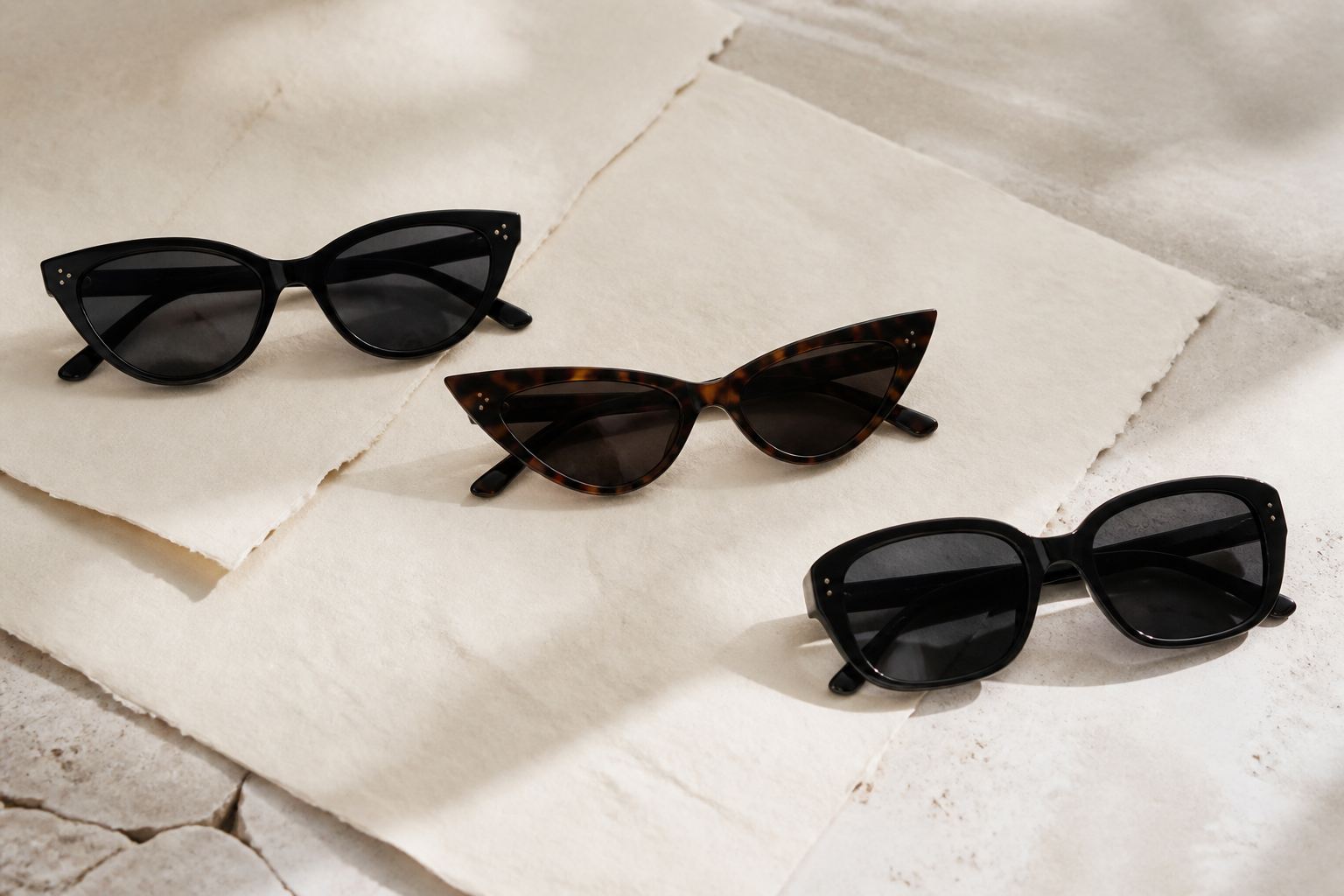 Three unbranded sunglasses shapes on cream paper showing a soft cat-eye, dramatic cat-eye and squoval frame
