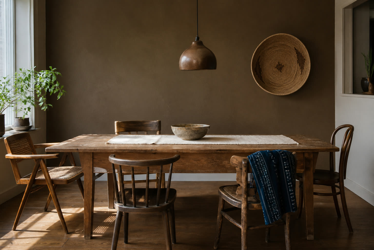 Dining room with a weathered timber table, mismatched vintage chairs, an indigo textile and woven wall piece