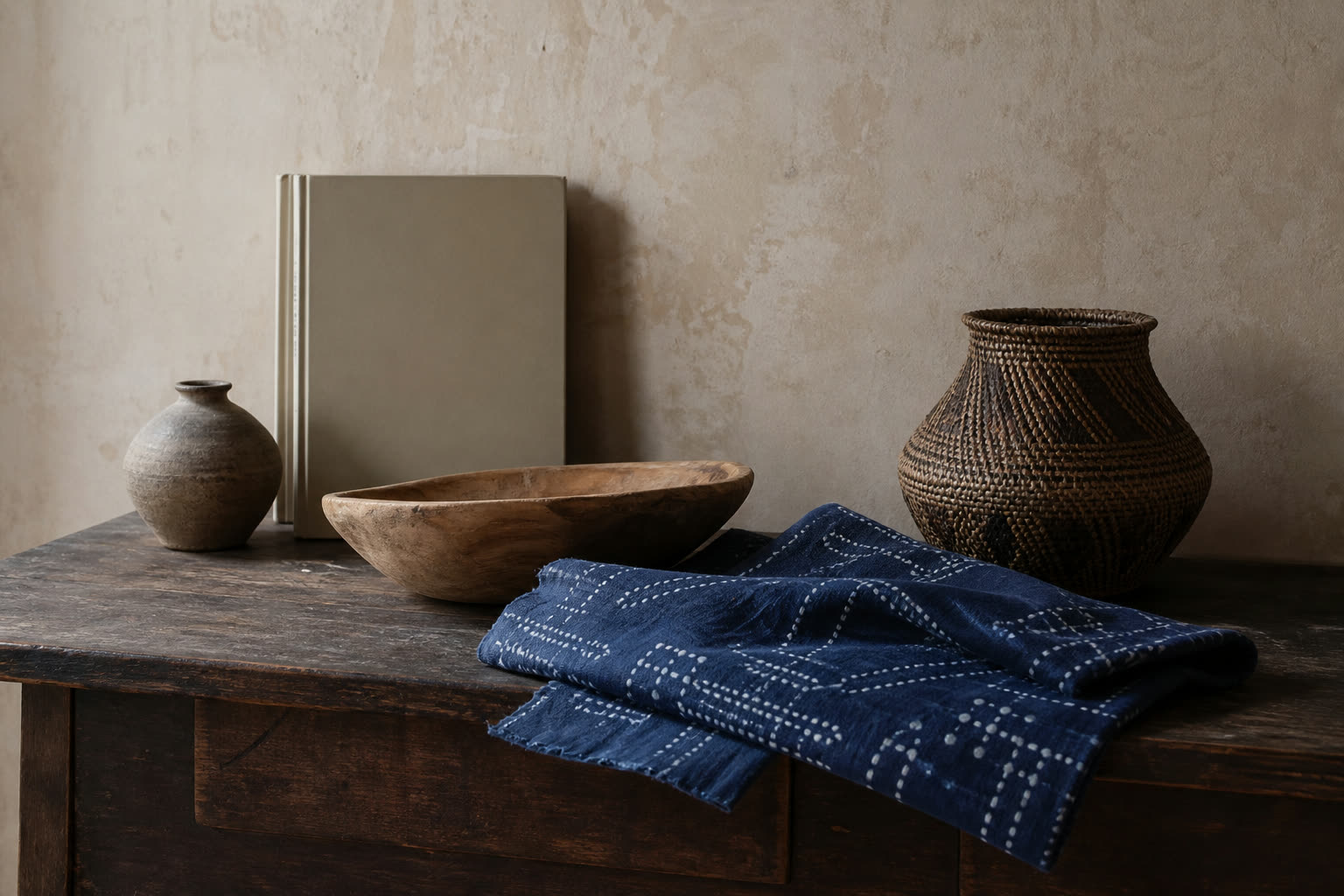 Indigo resist-dyed cotton, a carved timber bowl, woven basket and hand-thrown pottery on a worn oak console