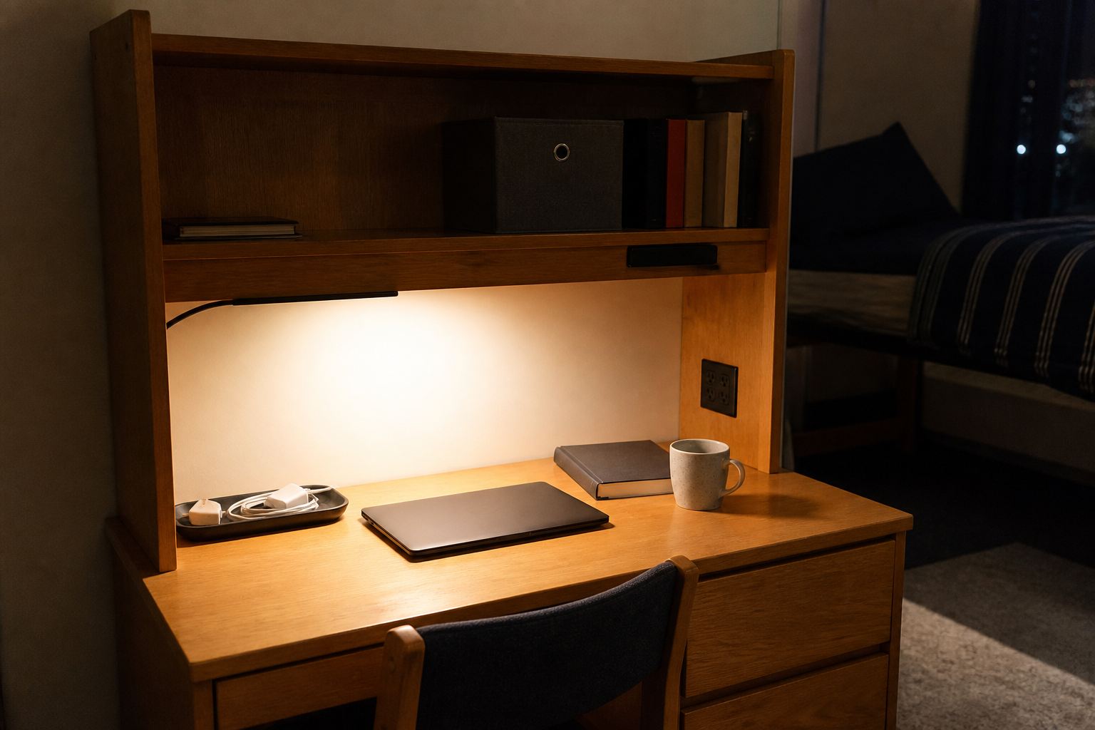 Dorm desk hutch at night with practical warm task lighting, controlled charging cables and an uncluttered worktop
