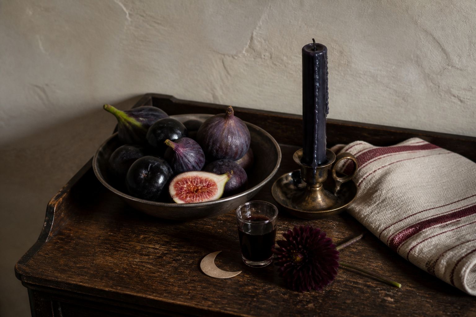 Dark figs, plums, a black candle and striped linen arranged for an elegant Summerween table
