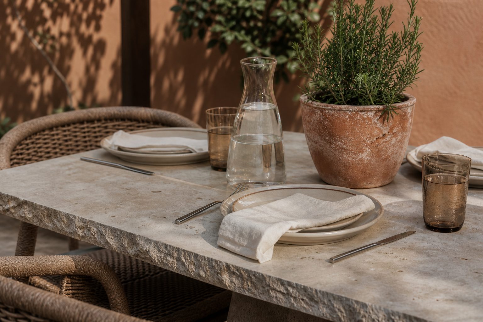 Outdoor dining table with ceramic plates, linen napkins, rosemary and stone surface