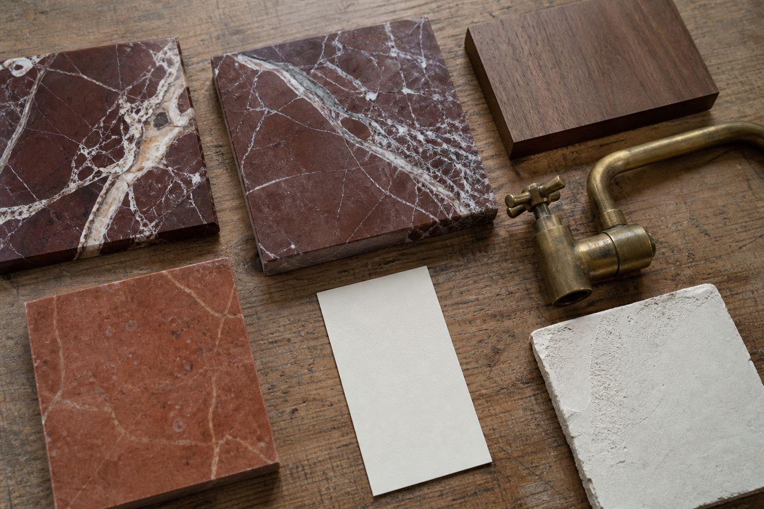 Red marble samples, walnut, aged brass, ivory plaster and grout colours arranged on a workshop table